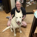 A woman sitting on the floor smiling with a large white dog sitting in front of her.